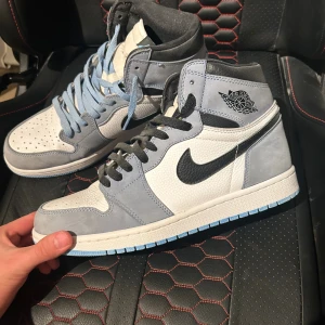 Nike Air Jordan 1 High grå/vit - Säljer ett par Nike Air Jordan 1 High med grå mockadetaljer, vit läderpanel och svart Swoosh. Skorna har blå och svarta skosnören samt blå yttersula. Klassisk Jordan Wings-logga på sidan och perforerad tå för extra stilpoäng.                                                                              Pris kan diskuteras 