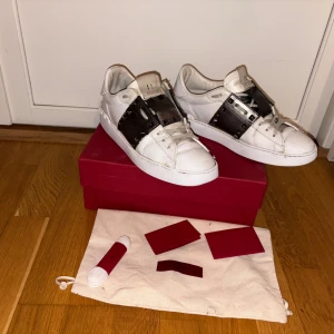 Valentino Rockstud  - Säljer ett par vita Valentino Rockstud sneakers med coola svarta skinnpaneler och ikoniska nitar över foten. Skorna har rund tå, platt sula och snörning. Alla spikar är hela. Og kan följa med vid snabb och smidig affär 