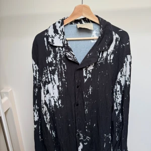 Svart och vit silkesskjorta Limitato - Unik svart och vit skjorta från Limitato i 100% silke med abstrakt mönster. Skjortan har klassisk krage, knappar framtill och lång ärm. Sval och lyxig känsla, perfekt för dig som gillar statement-plagg och exklusiva material.