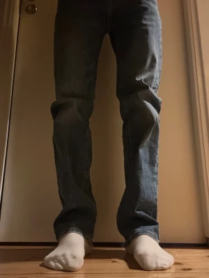 Blå raka jeans  - Säljer ett par klassiska blå jeans med rak passform och fyra fickor. Jeansen har en mörk tvätt med lätt slitning och är tillverkade i robust denim. Perfekt för dig som gillar en tidlös och enkel stil.