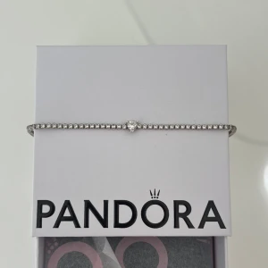 Pandora armband - Ett glittrigt armband från Pandora i silverfärg med små gnistrande stenar längs hela bandet och en hjärtformad sten i mitten. Bra skick, köp för ca 1100. Är öppen för prisförslag. Box ingår 