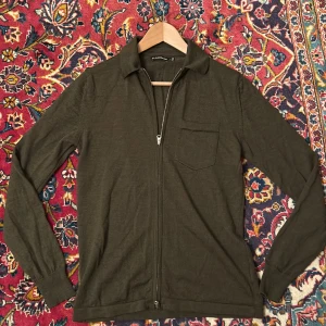 Mörkgrön zip-kofta från J.Lindeberg - Snygg mörkgrön kofta från J.Lindeberg i storlek S. Tröjan har dragkedja framtill, klassisk krage och en bröstficka. Materialet är mjukt och stickat, perfekt för lager-på-lager. Långärmad och stilren design som funkar till många looks.