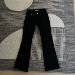 Svarta bootcut jeans med fickdetaljer - Svarta jeans från PellePelle med bootcut passform och snygga silvriga knappar på bakfickorna. Klassisk femficksmodell med markerade sömmar och bälteshällor. Perfekta för dig som gillar en stilren look med lite edge.