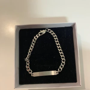 Silver Armband - 17cm. Stilrent ID-armband i silverfärg med platt bricka och grov kedja. Perfekt för att gravera med namn eller ett personligt budskap. Armbandet har en robust karbinlås och passar både tjejer och killar som gillar enkel och tidlös design. PRISET KAN DISKUTERAS.