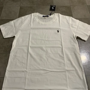 Vit t-shirt från Polo Ralph Lauren - Klassisk vit t-shirt från Polo Ralph Lauren i mjuk bomull. T-shirten har rund halsringning, korta ärmar och den ikoniska broderade loggan på bröstet. Perfekt basic-plagg med stilren design och skön passform.