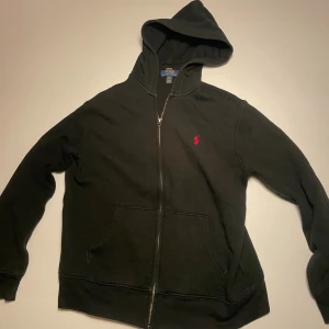 Svart hoodie från Polo Ralph Lauren - Svart hoodie från Polo Ralph Lauren med dragkedja och huva. Klassisk röd logga broderad på bröstet och stora fickor framtill. Perfekt för en chill och stilren look. Lite liten i stolek men funkar bra, helt okej andvänd. Priset kan diskuteras 