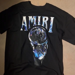 Svart Amiri t-shirt - Svart t-shirt från Amiri med stort grafiskt tryck framtill i blå, vit och svart. Trycket har coola detaljer och texten AMIRI i färgglada bokstäver. 