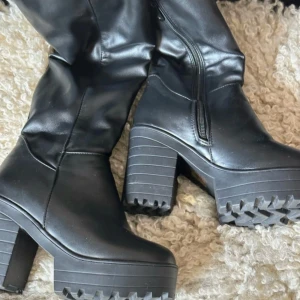 Snygga overknee stövlar - Snygga svarta overknee stövlar jättefint skick! Som nya, bara använda 1ggr Dom har en dragkedja på insidan och dom är fodrade med ett mönstrat mjukt innerfoder Platåklacken/sulan är tillverkad i gummi Skafthöjd 44cm Klackhöjd 9cm Sulans höjd 3cm Det är storlek 35,5- liten 36