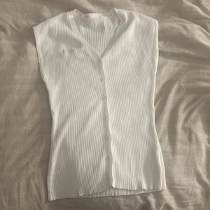 Vit ribbad ärmlös blus med knappar från shein - Säljer en fräsch vit ribbad blus med v-ringning och knappar framtill. Toppen är ärmlös och har en smickrande passform som passar perfekt till jeans eller kjol. Enkel och stilren design som är lätt att matcha.