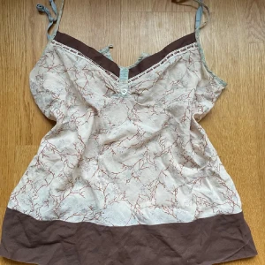 linnetopp med mönster - Säljer en beige linnetopp med brunt kantband och botten, tunna axelband och ett unikt grenliknande mönster i brunt. Storlek S/M💕