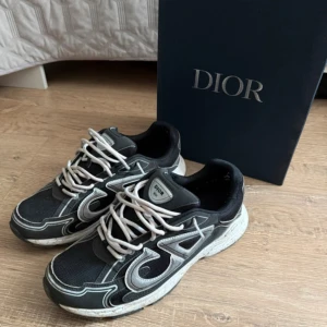 B30 skor - Säljer ett par svarta B30 sneakers med vita och grå detaljer. Skorna har en chunky sula, mesh och syntetmaterial samt tydlig CD logga på sidan. Vita snören och sportig vibe, perfekta för dig som gillar exklusiva streetwear-sneakers.