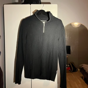 Svart ribbad half zip från Jack & Jones - Svart långärmad tröja från Jack & Jones med ribbad struktur och half zip-dragkedja i halsen. Tröjan har en stilren, smal passform och är tillverkad i mjuk bomull. Perfekt för dig som gillar minimalistisk och clean stil.