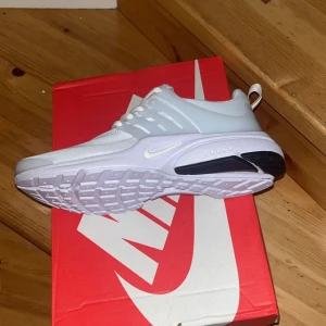 Nike Presto vita sneakers - Fräscha Nike Presto sneakers i helvitt med stilren design och diskret Swoosh-logga. Ovandelen är i mesh och syntet för en luftig känsla och skön passform. Sulan är vit med svarta detaljer undertill och skon har snörning för bästa komfort.