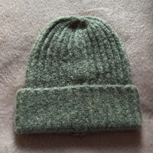 Grön ribbad mössa från Pieces - Mysig grön mössa från Pieces med ribbad struktur och bred uppvikt kant. Perfekt för kyliga dagar och enkel att matcha med din jacka. Materialet känns mjukt och värmande, och färgen är diskret men ändå trendig.