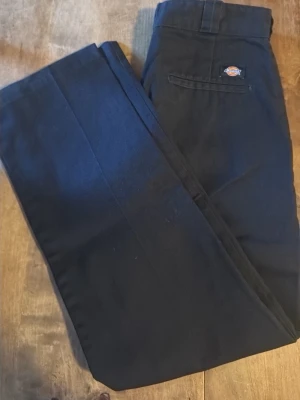 Svarta Dickies 874 byxor W31/L32 - Klassiska svarta Dickies 874 byxor med rak passform och stilren look. Byxorna har en enkel bakficka med Dickies-logga och är gjorda i slitstarkt material av polyester och bomull. Perfekta för dig som gillar streetwear 