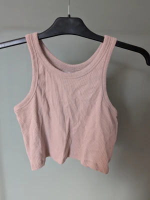Beige ribbad linnetopp från 157 - Säljer en croppad, ribbad linnetopp i beige från 157. Toppen är ärmlös med breda axelband och rund halsringning. Perfekt för varma dagar eller som lager under skjorta. Enkel och stilren design som är lätt att matcha.