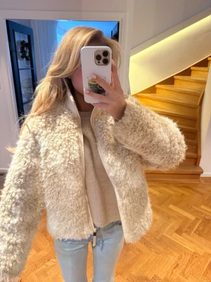 Beige teddyjacka med dragkedja - Supermysig beige teddyjacka med fluffig struktur och dragkedja framtill. Jackan har en rak passform och hög krage som håller dig varm. Perfekt att slänga på sig över en hoodie eller stickad tröja. Enkel att matcha med jeans eller kjol.