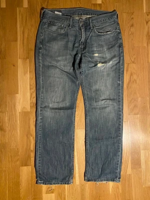 Levi's 514 jeans - Klassiska blå Levi's 514 jeans med rak passform och slitna detaljer. Jeansen har fem fickor, dragkedjegylf och råa kanter vid benslut. Ifall fler frågor eller bilder skriv!