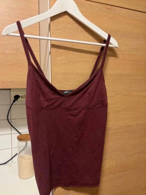 Vinröd linnetopp från Zara - Säljer en enkel och snygg vinröd linnetopp från Zara. Toppen har tunna axelband och en mjuk, något draperad urringning. Perfekt att matcha med jeans eller kjol för en chill look.