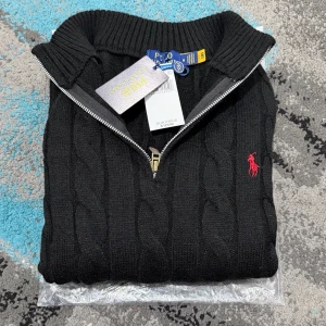 Svart Zip Knit Polo Ralph Lauren - Zip-Knkt svart tröja från Polo Ralph Lauren med halv dragkedja och röd broderad logga på bröstet. Tröjan har ribbade muddar och hög krage, perfekt för kyliga dagar. Klassisk och stilren design som funkar till allt. TVEKA INTE ATT SKICKA EN BUD:)