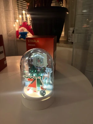 Jul lampa  - juldekoration från IKEA:s STRÅLA-serie med motiv av granar, ren och tomte under en glaskupa.