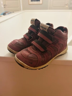 Lila sneakers från Viking strl 32 - Säljer ett par vinröda sneakers från Viking i storlek 32. Skorna har två kardborreband, meshdetaljer för extra ventilation och en robust sula med bra grepp. Perfekta för aktiva dagar och passar till många olika outfits.
