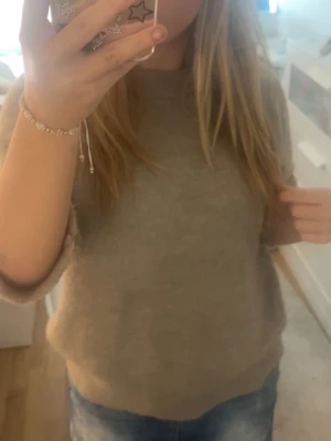 Beige stickad tröja med kort ärm - Mysig beige stickad tröja med rund hals och ärmar som går ner till armbågen. Perfekt för kyliga dagar och enkel att matcha med jeans eller andra favoritplagg. Tröjan har en normal passform och är tillverkad i ett mjukt stickat material.