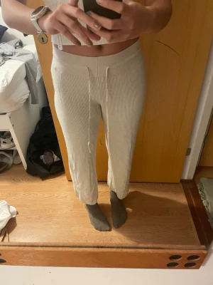Beige ribbade mjukisbyxor från Uniqlo - Säljer ett par beige ribbade mjukisbyxor från Uniqlo i storlek L. Byxorna har snörning i midjan, croppad längd och är tillverkade av en mjuk blandning av bomull, polyester, rayon och nylon. Perfekta för chill dagar och riktigt sköna att ha på sig. Passar även för S