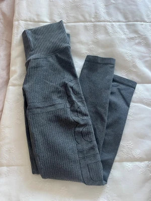 Grå ribbade leggings  - Säljer ett par mörkgrå leggings med ribbad struktur och hög midja som sitter riktigt skönt. Materialet är stretchigt och passar perfekt till träning eller chill. Aim’n ogga på benet för en clean look.