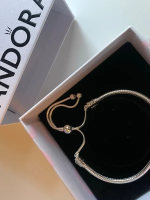 Säljer Pandora silverarmband - Snyggt och stilrent armband från Pandora i silverfärg. Ormkedja med justerbar låsning och två små kulor i ändarna. Kommer i originalask med silkespapper. Perfekt accessoar för att lyfta din outfit.