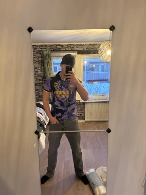 Lila Real Madrid Adidas t-shirt - Säljer en lila Real Madrid t-shirt från Adidas med coolt grafiskt mönster och gula detaljer. Tröjan har korta ärmar, svart krage och gula ränder på axlarna. Perfekt för dig som älskar fotboll och vill sticka ut med en snygg supportertröja.