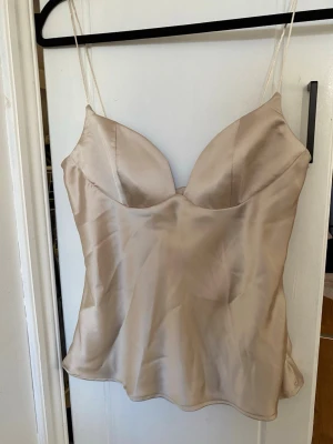Festtopp från zara - Säljer en champagnefärgad linne-topp i satin med tunna axelband och snygg v-ringad urringning med mjukt tyg. Har även en dragkedja på ena sidan för bästa passform. Skriv om frågor och gärna innan du trycker på köp💞 säljer på grund av att jag köpte fel storlek därför är den helt oanvänd endast provad, med prislapp kvar!