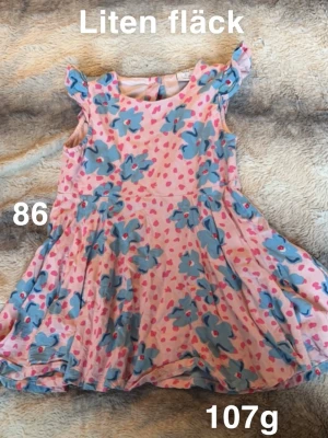 Rosa blommig klänning med volangärm - Supersöt rosa klänning med blå blommor och små rosa hjärtan. Klänningen har volangärmar och en snurrig kjol, perfekt för lek och bus. lätt att röra sig i. 🌸En liten fläck. Storlek 86 