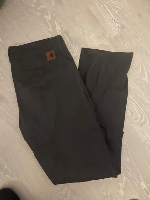 Svarta Carhartt Club Pant 33/32 - Säljer ett par svarta Carhartt Club Pant i storlek 33/32. Byxorna har en klassisk rak passform och är tillverkade i 100% bomull med fickfoder i bomull och polyester. Snygg Carhartt-logga på bakfickan och stilren look.