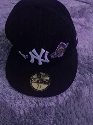  New Era 59FIFTY Yankees keps - Säljer en svart New Era 59FIFTY keps med New York Yankees-logga framtill och broderad World Series-patch på sidan. Klassisk rak skärm och MLB-logga bak. Tillverkad i 100% polyester och passar dig som gillar sportig streetstyle.