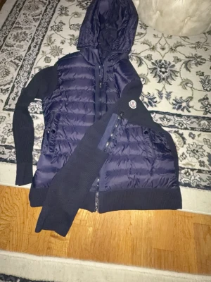 Mörkblå Moncler pufferjacka med huva - Säljer en mörkblå pufferjacka från Moncler med stickade ärmar och huva. Jackan har dragkedja framtill, två fickor med dragkedja och Moncler-logga på ena ärmen. Perfekt för dig som vill ha en snygg och sportig look under höst och vinter.NFC FUNKAE ! Pris kan diskuteras