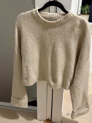 Beige croppad stickad tröja Bershka - Mysig beige croppad stickad tröja från Bershka. Tröjan har rund halsringning, ribbade muddar och långa ärmar. Perfekt för lager på lager och chill dagar. Passar dig som gillar en enkel men trendig look.