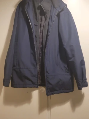 Blå vinterjacka från Weatherproof - Mörkblå vinterjacka från Weatherproof med quiltat foder och dragkedja framtill. Jackan har hög krage och är perfekt för kalla dagar. Klassisk och stilren design som funkar till det mesta.