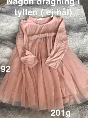 Rosa tyllklänning med lång ärm - Supersöt rosa klänning med långärmad överdel och fluffig kjol i tyll. Perfekt för dig som gillar volym och en romantisk look. Kjolen har flera lager tyll som ger extra snurr och en söt detalj i midjan.🌸Fint använt skick. Någon dragning finns. Storlek 92