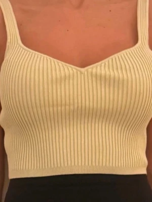 Ribbad beige linnetopp - Snygg ribbad linnetopp i beige med breda axelband och croppad passform. Toppen har en lätt v-ringad halsringning och är tillverkad i ett stretchigt stickat material som sitter skönt på kroppen. Perfekt för varma dagar eller som layering-plagg.