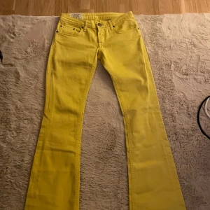 Gula bootcut jeans från Dondup - Säljer ett par riktigt snygga gula jeans från Dondup i klassisk bootcut-modell. Byxorna har fem fickor, bälteshällor och coola detaljer bak med broderade fickor. Materialet är bomull och de har en skön passform som sitter snyggt över höfterna.