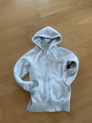 Russemerch zip up hoodie - Snygg grå ZipUp russemerch-hoodie i mycket fint skick. Bekväm passform med mjukt material som funkar perfekt både till vardags och för att visa russestilen. Stilren, lättmatchad och redo för ny ägare – ett måste för dig som vill ha en clean men trendig hoodie. 🔥