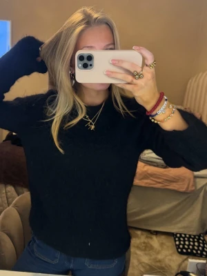 Svart stickad mohair tröja  - Mysig svart stickad tröja med lång ärm och rund hals. Perfekt att slänga på sig till jeans för en enkel och stilren look. Tröjan har en klassisk passform och är superenkel att matcha med olika outfits. Har ett hål i ärmen 