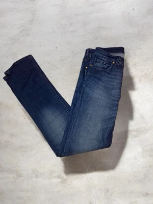 mörkblå jeans från denim birds  - Snygga denim birds jeans i mörkblå tvätt med klassiska fem fickor och guldfärgade nitar. Jeansen har rak passform och är tillverkade i slitstarkt denimtyg av bomull. Perfekta för dig som gillar en tidlös och clean look.