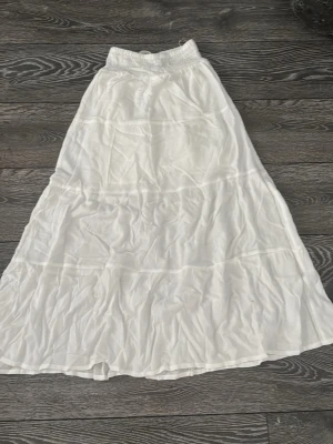 Vit långkjol från H&M med resår - Säljer en vit långkjol från H&M med bred resår i midjan. Kjolen är tillverkad i ett tunt och lätt tyg som ger en luftig känsla. Perfekt för varma dagar och enkel att matcha med olika toppar.