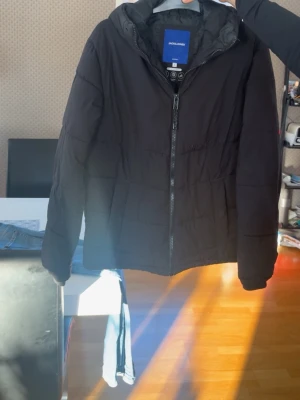 Svart pufferjacka från Jack & Jones - Säljer en svart pufferjacka från Jack & Jones i storlek S. Jackan har huva, quiltad design och dragkedja framtill. Perfekt för kalla dagar och har en clean look som funkar till det mesta. Tillverkad i polyester för extra värme och komfort.