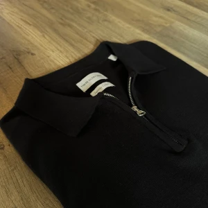 Svart långärmad tröja polo/pike med halv dragkedja - Svart långärmad tröja från These Glory Days med klassisk krage och halv dragkedja framtill. Tillverkad i bomull, perfekt för en clean och stilren look. Passformen är normal och materialet känns mjukt mot huden.