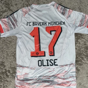 FC Bayern München bortatröja Olise 17 - Säljer en FC Bayern München bortatröja från Adidas i storlek S. Tröjan är vit med digitalt mönster i rött och grått, har korta ärmar och klubbmärke samt sponsortryck på bröstet. Namn och nummer Olise 17 på ryggen. Tillverkad i lätt och ventilerande polyester.