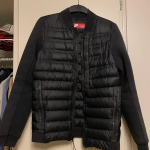 Svart pufferjacka från Nike - Säljer en svart pufferjacka från Nike med quiltad framsida och baksida. Jackan har långa ärmar i mjukt material, dragkedja framtill och två sidofickor med dragkedja. Perfekt för kyliga dagar och har en clean, sportig look. Storlek S/XS 