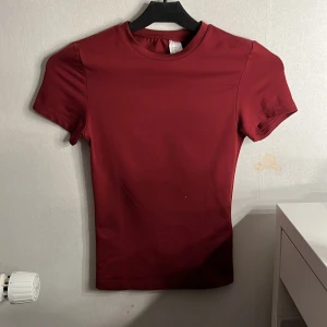 Vinröd tight t-shirt XXS - Enkel och stilren vinröd t-shirt i tight passform. T-shirten har rund halsringning och korta ärmar. Perfekt basplagg i garderoben och lätt att matcha med andra kläder. Testat en gång, nyskick!